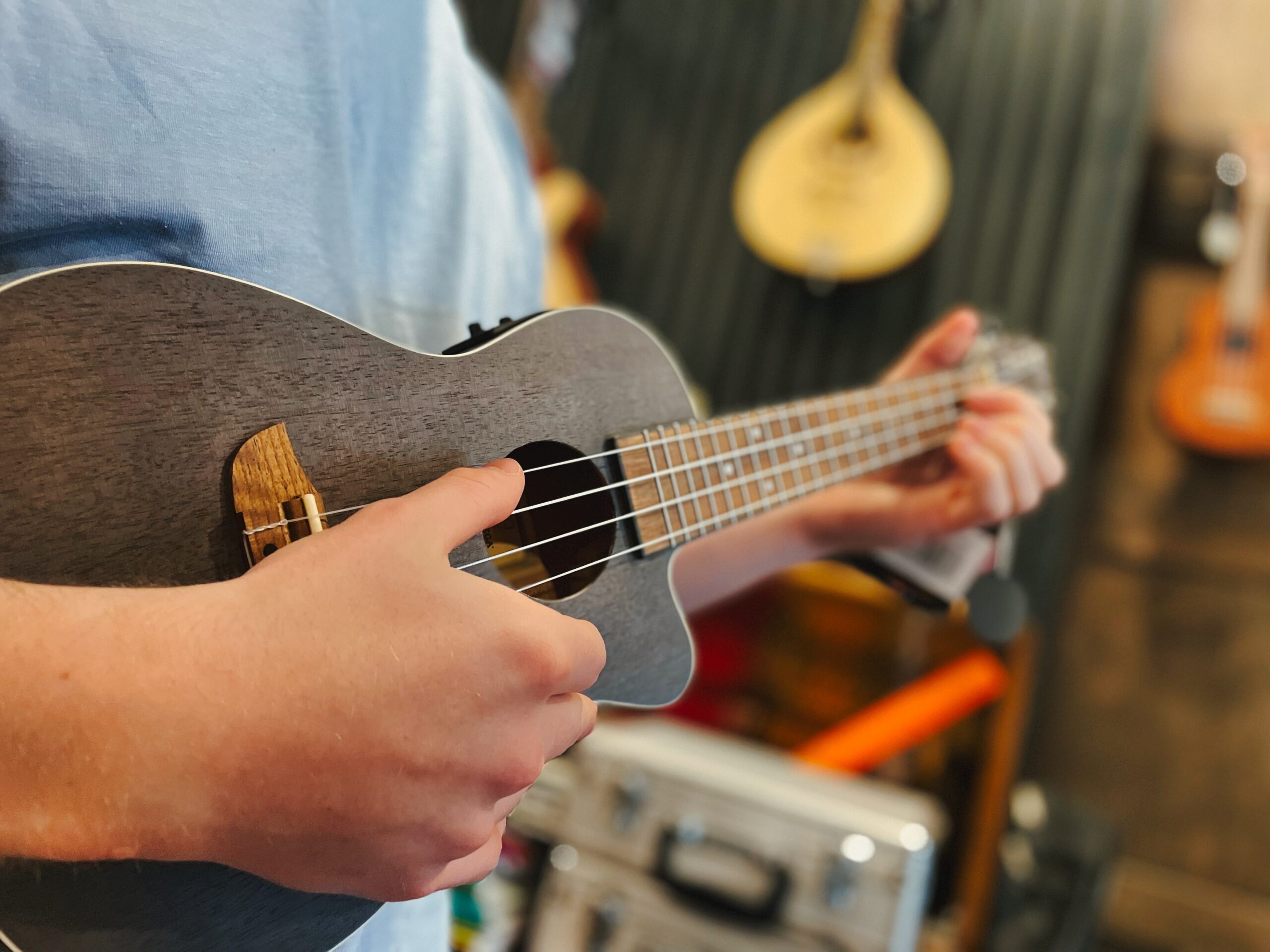 A man in a blue t-shirt playing a coal-black Ortega ukulele in a music shop