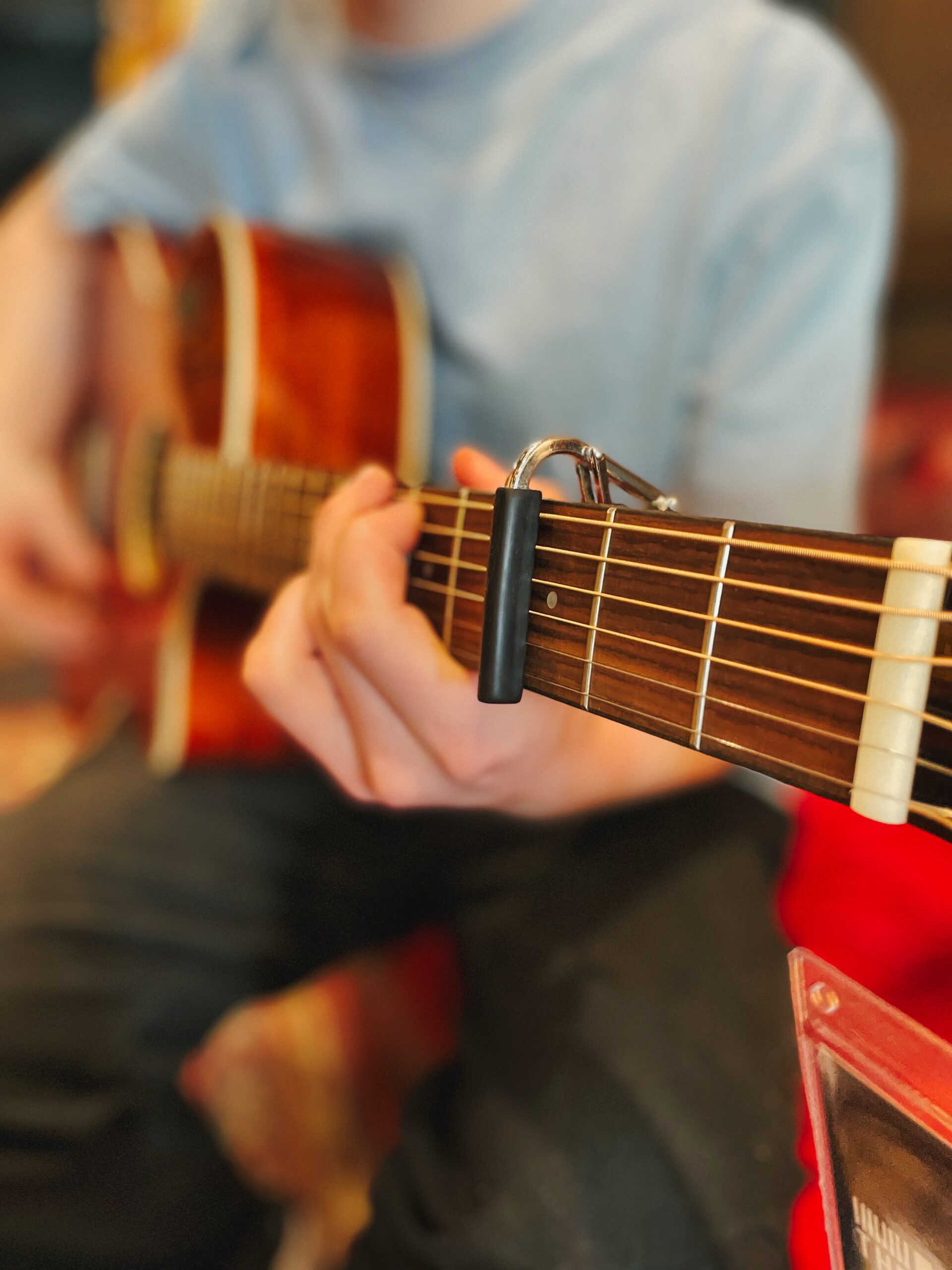 Seated male playing acoustic guitar with capo close up. Strumming chords in a music lesson