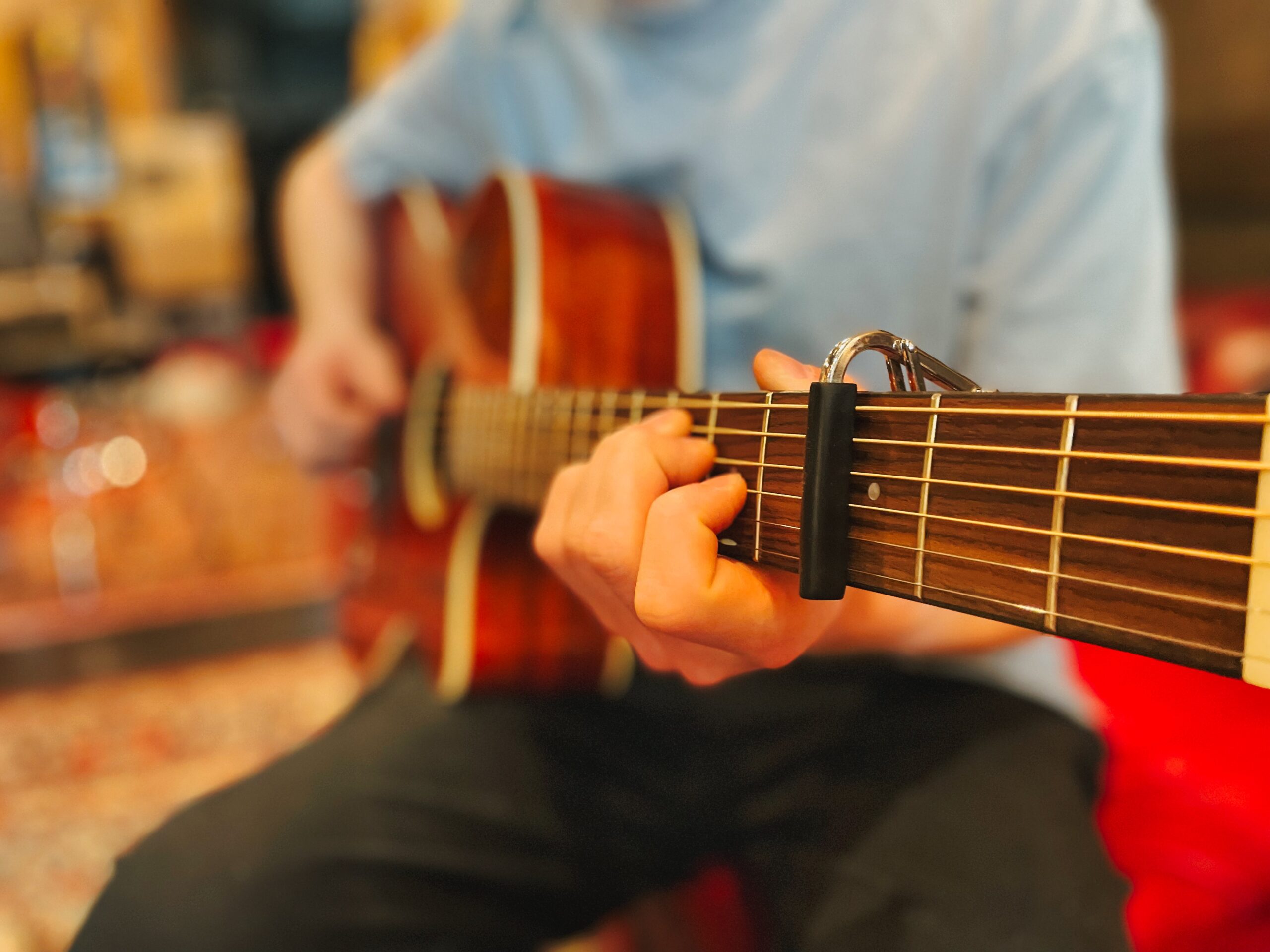 Male playing acoustic guitar fitted with a capo - music lesson